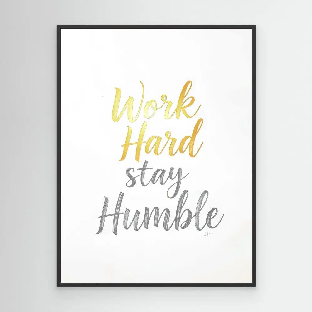 A framed motivational print featuring the text ’Work Hard stay Humble’ in gold and gray lettering.